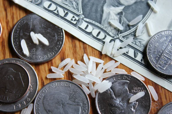 Dollar coins and dollar bills are scattered on a wooden table with grains of rice.