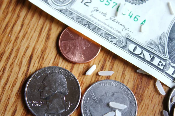 Dollar coins and dollar bills are scattered on a wooden table with grains of rice.