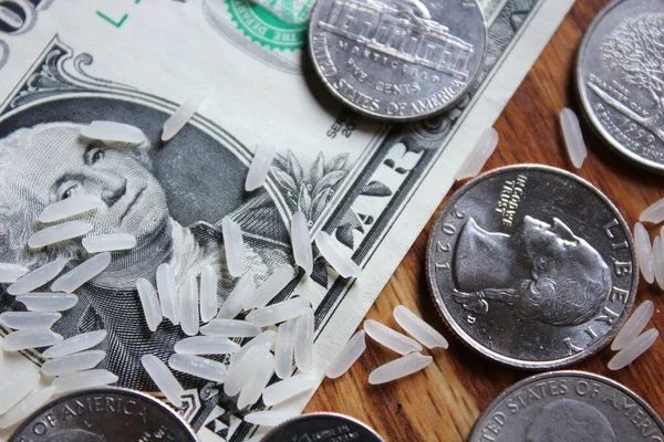 Dollar coins and dollar bills are scattered on a wooden table with grains of rice.