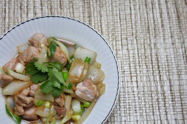 Kızarmış domuz eti ile soğan ve taze soğan karışımı beyaz tabakta servis edilen Tayland yemeği Taylandlıların yediği popüler bir yemektir..