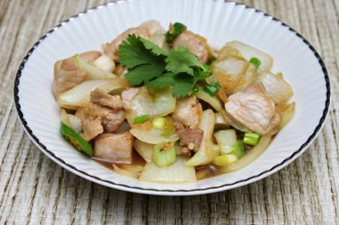 Kızarmış domuz eti ile soğan ve taze soğan karışımı beyaz tabakta servis edilen Tayland yemeği Taylandlıların yediği popüler bir yemektir..