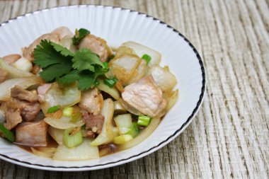 Kızarmış domuz eti ile soğan ve taze soğan karışımı beyaz tabakta servis edilen Tayland yemeği Taylandlıların yediği popüler bir yemektir..