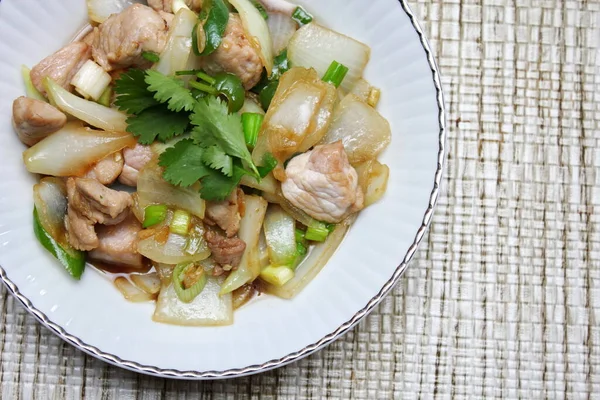 Kızarmış domuz eti ile soğan ve taze soğan karışımı beyaz tabakta servis edilen Tayland yemeği Taylandlıların yediği popüler bir yemektir..