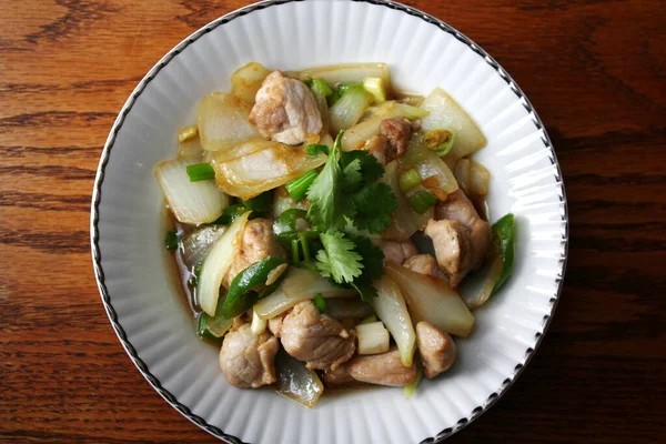 Kızarmış domuz eti ile soğan ve taze soğan karışımı beyaz tabakta servis edilen Tayland yemeği Taylandlıların yediği popüler bir yemektir..