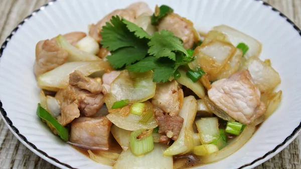 Kızarmış domuz eti ile soğan ve taze soğan karışımı beyaz tabakta servis edilen Tayland yemeği Taylandlıların yediği popüler bir yemektir..