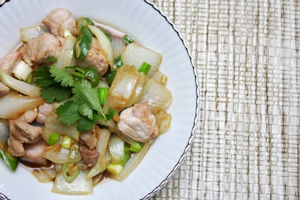 Kızarmış domuz eti ile soğan ve taze soğan karışımı beyaz tabakta servis edilen Tayland yemeği Taylandlıların yediği popüler bir yemektir..