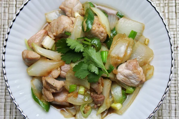 Kızarmış domuz eti ile soğan ve taze soğan karışımı beyaz tabakta servis edilen Tayland yemeği Taylandlıların yediği popüler bir yemektir..