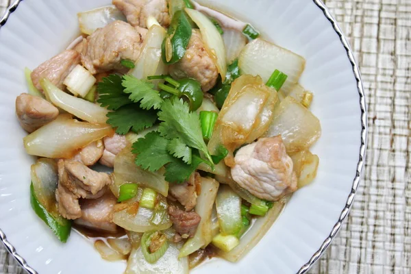 Kızarmış domuz eti ile soğan ve taze soğan karışımı beyaz tabakta servis edilen Tayland yemeği Taylandlıların yediği popüler bir yemektir..