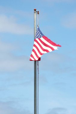 Bayrağın ucunda eski bir Amerikan bayrağı Rüzgarda dalgalanan bayrak direğinde mavi bir gökyüzü arka planında.