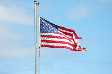 Bayrağın ucunda eski bir Amerikan bayrağı Rüzgarda dalgalanan bayrak direğinde mavi bir gökyüzü arka planında.