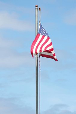 Bayrağın ucunda eski bir Amerikan bayrağı Rüzgarda dalgalanan bayrak direğinde mavi bir gökyüzü arka planında.