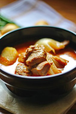 Kahverengi ahşap bir masada haşlanmış patates ve biberle servis edilen siyah tabakta servis edilen körili masaj..