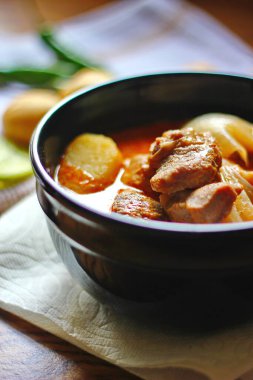 Kahverengi ahşap bir masada haşlanmış patates ve biberle servis edilen siyah tabakta servis edilen körili masaj..