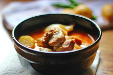 Kahverengi ahşap bir masada haşlanmış patates ve biberle servis edilen siyah tabakta servis edilen körili masaj..