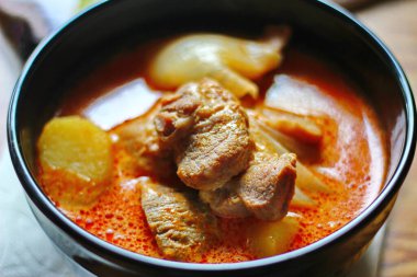 Kahverengi ahşap bir masada haşlanmış patates ve biberle servis edilen siyah tabakta servis edilen körili masaj..