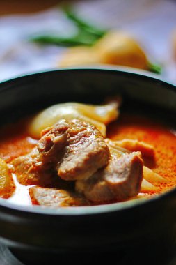 Kahverengi ahşap bir masada haşlanmış patates ve biberle servis edilen siyah tabakta servis edilen körili masaj..