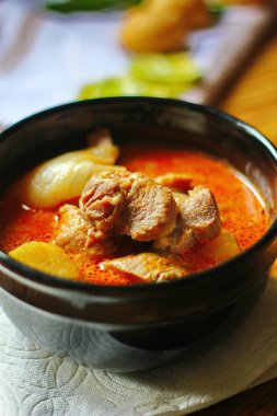 Kahverengi ahşap bir masada haşlanmış patates ve biberle servis edilen siyah tabakta servis edilen körili masaj..