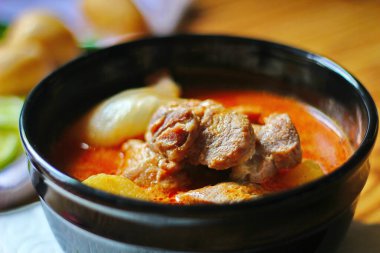 Kahverengi ahşap bir masada haşlanmış patates ve biberle servis edilen siyah tabakta servis edilen körili masaj..