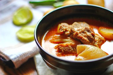 Kahverengi ahşap bir masada haşlanmış patates ve biberle servis edilen siyah tabakta servis edilen körili masaj..