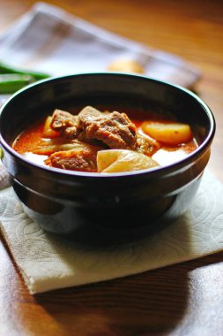 Kahverengi ahşap bir masada haşlanmış patates ve biberle servis edilen siyah tabakta servis edilen körili masaj..