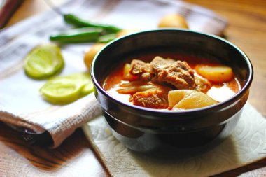 Kahverengi ahşap bir masada haşlanmış patates ve biberle servis edilen siyah tabakta servis edilen körili masaj..