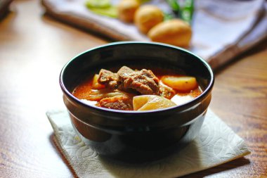 Kahverengi ahşap bir masada haşlanmış patates ve biberle servis edilen siyah tabakta servis edilen körili masaj..