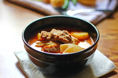 Kahverengi ahşap bir masada haşlanmış patates ve biberle servis edilen siyah tabakta servis edilen körili masaj..