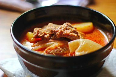 Kahverengi ahşap bir masada haşlanmış patates ve biberle servis edilen siyah tabakta servis edilen körili masaj..