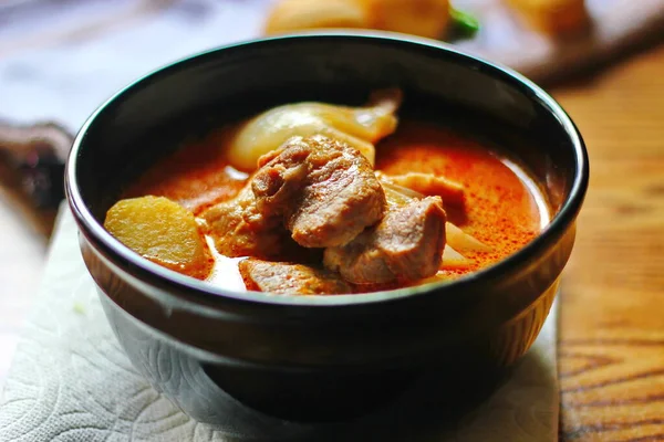 Kahverengi ahşap bir masada haşlanmış patates ve biberle servis edilen siyah tabakta servis edilen körili masaj..