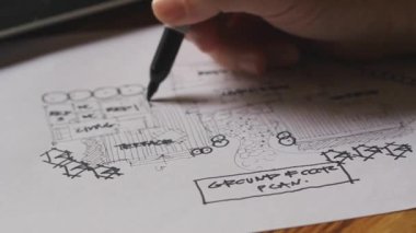 An architect sketching a residential building plan on white paper at a wooden table.