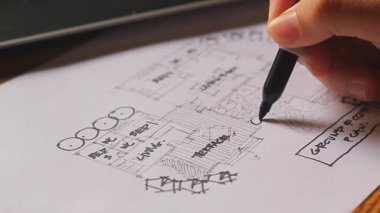 An architect sketching a residential building plan on white paper at a wooden table.