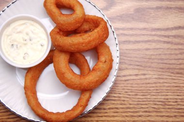 Soğan halkaları aperatif olarak tabakta ve restoran menüsünün bir parçası olarak, beyaz bir tabakta ahşap bir masada sunuluyor. Fotoğraf yukarıdan, düz konumda.