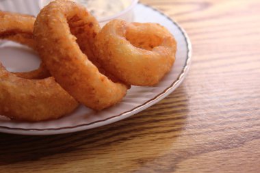 Ev yapımı kızarmış soğan halkaları ve ahşap masanın üzerindeki sos tabağı yakın plan.