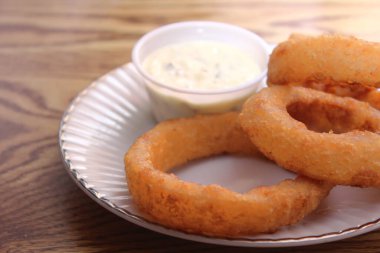 Ev yapımı kızarmış soğan halkaları ve ahşap masanın üzerindeki sos tabağı yakın plan.