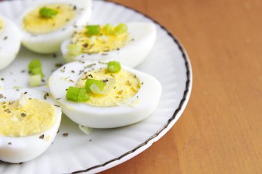 Yarısı haşlanmış yumurta, dilimlenmiş taze soğanla süslenmiş. Beyaz bir tabakta servise hazır.