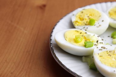 Yarısı haşlanmış yumurta, dilimlenmiş taze soğanla süslenmiş. Beyaz bir tabakta servise hazır.