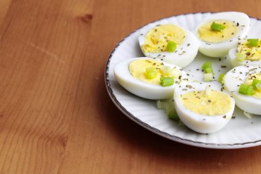 Yarısı haşlanmış yumurta, dilimlenmiş taze soğanla süslenmiş. Beyaz bir tabakta servise hazır.