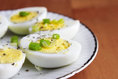 Yarısı haşlanmış yumurta, dilimlenmiş taze soğanla süslenmiş. Beyaz bir tabakta servise hazır.