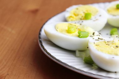 Yarısı haşlanmış yumurta, dilimlenmiş taze soğanla süslenmiş. Beyaz bir tabakta servise hazır.