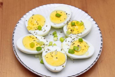 Yarısı haşlanmış yumurta, dilimlenmiş taze soğanla süslenmiş. Beyaz bir tabakta servise hazır.