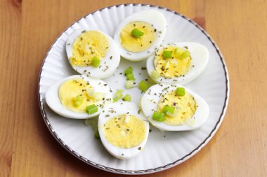 Yarısı haşlanmış yumurta, dilimlenmiş taze soğanla süslenmiş. Servise hazır beyaz bir tabakta, Düz yatıyordu, Üst Manzara.