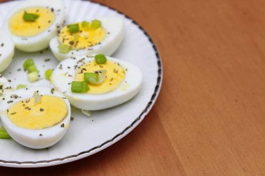 Yarısı haşlanmış yumurta, dilimlenmiş taze soğanla süslenmiş. Beyaz bir tabakta servise hazır.