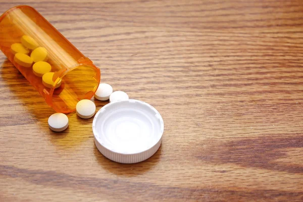 Pills were poured from the orange pill bottle onto the wooden table, medicine pill on wooden table..