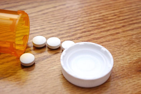 Pills were poured from the orange pill bottle onto the wooden table, medicine pill on wooden table.