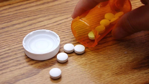 A man's hand is taking pills from an orange pill bottle on a wooden table, medicine pill on wooden table.