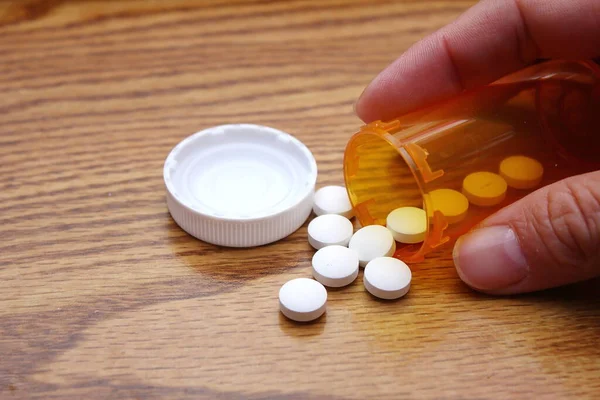 A man\'s hand is taking pills from an orange pill bottle on a wooden table, medicine pill on wooden table.