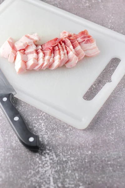 Seri domuz eti mutfakta beyaz bir doğrama tahtasıyla dilimlenir. Domuzu çiğ olarak kes.