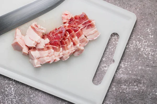 Seri domuz eti mutfakta beyaz bir doğrama tahtasıyla dilimlenir. Domuzu çiğ olarak kes.