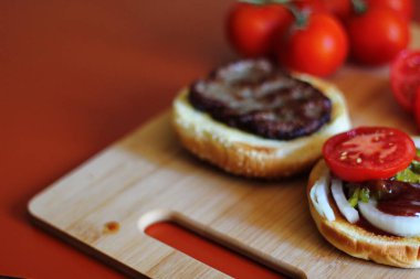 Hamburger dilimlenmiş domates, soğan ve turşuyla servis ediliyor. Mutfaktaki tahta kesme tahtasının üzerinde.
