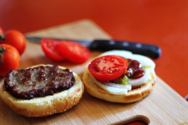 Hamburger dilimlenmiş domates, soğan ve turşuyla servis ediliyor. Mutfaktaki tahta kesme tahtasının üzerinde.